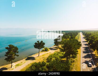 Aerial panning view scenic Sevan lake panorama with pine trees and beach in sunny summer day. Armenia holiday destination. Gegharkunik province Stock Photo