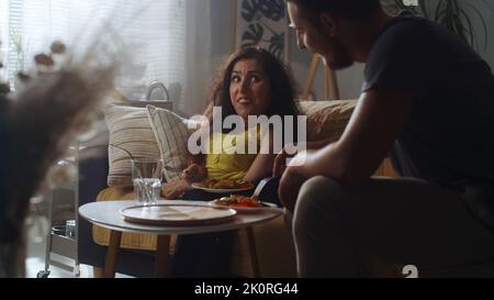 Woman with a physical disability and man joking and laughing together while sitting on a couch and having a dinner at home Stock Photo