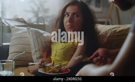 Wife with a spinal muscular atrophy and husband smiling and having conversation during eating a tasty dinner in living room on a sofa Stock Photo