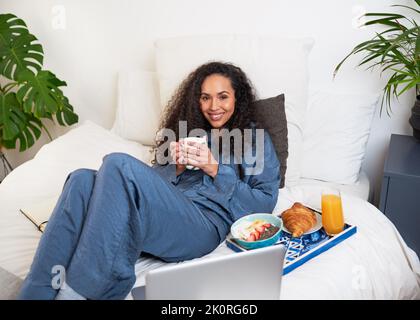 A young woman watches movies in bed while having brunch as self care Stock Photo