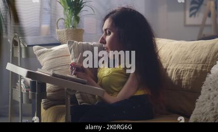 Woman with a disability smiling while drawing on digital tablet computer with stylus sitting on a couch at home Stock Photo