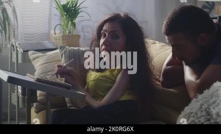 Woman with a disability drawing on digital tablet computer using pencil and talking with husband while sitting on a couch at the table at home Stock Photo