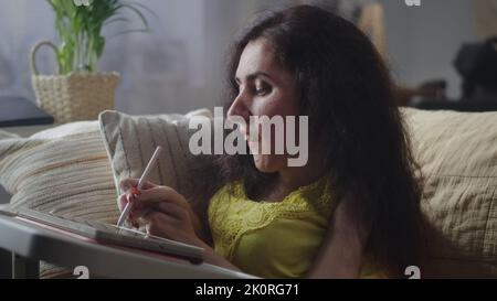 Woman with a disability smiling while drawing on digital tablet computer with stylus sitting on a couch at home Stock Photo