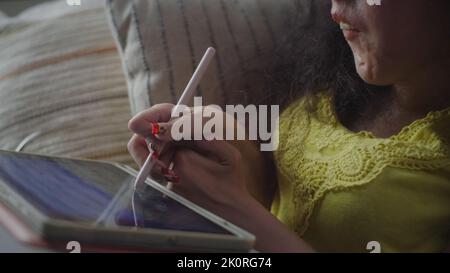 Woman with a disability smiling while drawing on digital tablet computer with stylus sitting on a couch at home Stock Photo