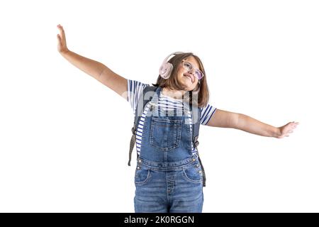 Young female student with backpack has headphones on and arms wide apart dreaming looking up. Stock Photo