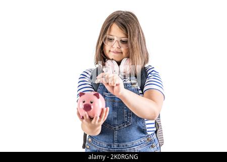 Young girl in glasses puts a coin into a piggybank. Stock Photo