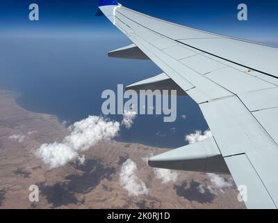 View of a section of the airplane wing and beautiful floating clouds as seen from an airplane window during mid flight. Stock Photo