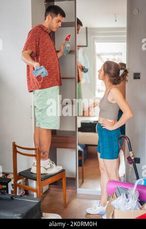 Young adults, a woman and a man clean shelv with mirror together. The concept of a shared lifestyle. Stock Photo