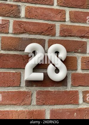 Number 28 in a smooth shape, made of white ceramic on some old red bricks Stock Photo