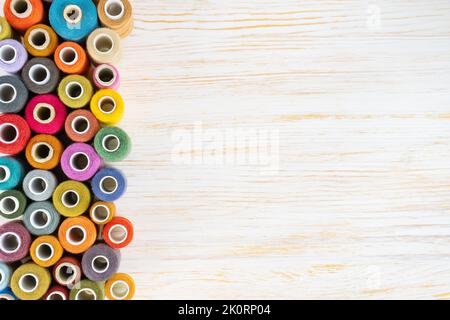 Sewing thread spools multicolored background, scattering of various colors sewing threads, colored yarns on white wooden surface with copy space. Flat Stock Photo