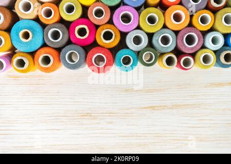 Sewing thread spools multicolored background, scattering of various colors sewing threads, colored yarns on white wooden surface with copy space. Flat Stock Photo