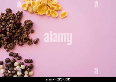 top view of corn flakes near cereal balls with vanilla and chocolate flavors and granola isolated on pink,stock image Stock Photo