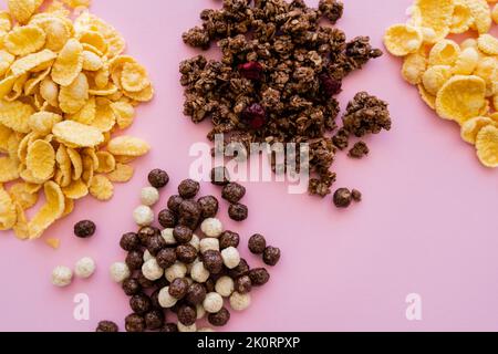 top view of corn flakes near cereal balls with vanilla and chocolate flavors and tasty granola isolated on pink,stock image Stock Photo