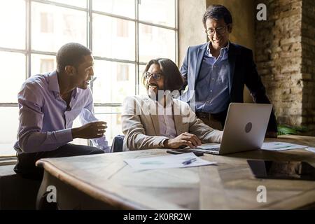 Three multiethnic young adult entrepreneurs colleagues smiling and talking about their business standing in front of a laptop computer in the office - Stock Photo