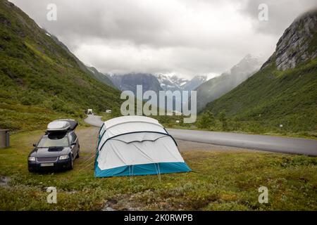 People, camping wild in Norway in high mountains, snow, cold, fog at night, pitched tent next to a car near the road Stock Photo