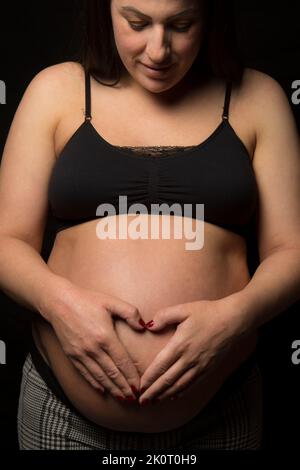 Young Brunette woman looking down at her big baby bump, studio light used. Stock Photo