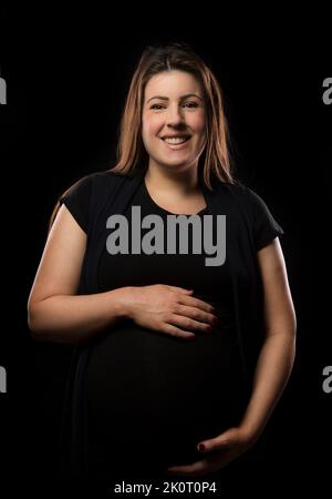 Young brunette woman at late stages of pregnancy smiles and poses with
