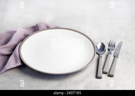 Table setting. White plate, cutlery and napkin on light gray background. Stock Photo