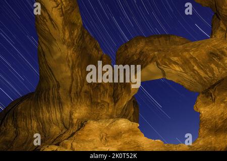 Star trails over Double Arch at night with artificial light painting with a hand-held spotlight.  Arches National Park, Moab, Utah. Stock Photo
