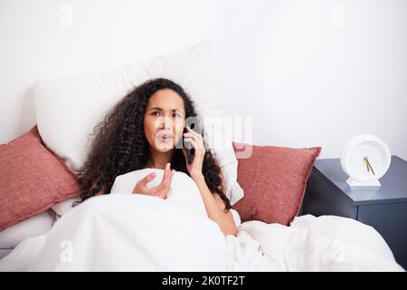 A young multi-ethnic woman gestures mid-conversation during call in bed Stock Photo