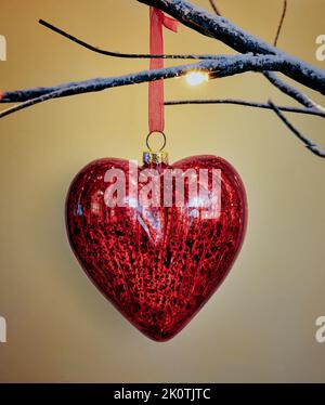 Hanging Christmas Tree Decoration in heart shape in traditional red and gold hanging on Twig tree Stock Photo