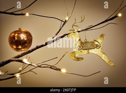 Gold reindeer decoration hanging from a modern Twig Tree Christmas Tree Decorated in traditional gold Stock Photo