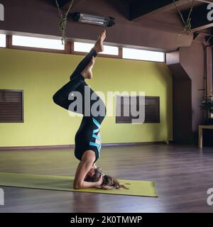 Woman practicing yoga, doing variation of shirshasana exercise, inverted asana, exercising on mat in studio Stock Photo