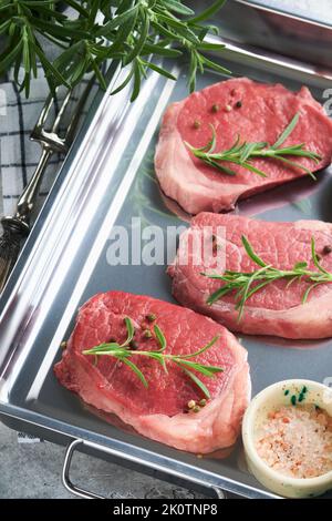 Steaks. Fresh Filet mignon Steaks with spices rosemary and pepper in kitchen tray on light gray background. Top view. Stock Photo