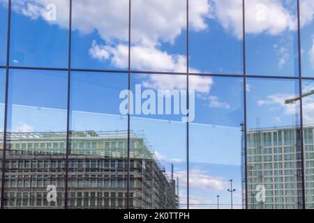 Reflection of a large construction site with new buildings and slightly cloudy sky in a glass facade of a modern building Stock Photo
