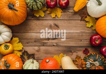 Autumn composition frame with variety of pumpkins, gourds, squash types, apples, kaki persimmon fruit, leaves. Fall flat lay, copy space on wood. Stock Photo
