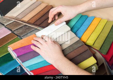 Man chooses samples of colored fabric on table close up Stock Photo