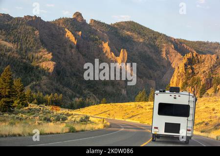 A camper trailer on a highway at sunrise in the Absaroka Mountains traveling along the North Fork of the Shoshone River, headed to Yellowstone Park. Stock Photo