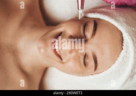 Freckled woman face receiving mesotherapy injection with derma pen on face for rejuvenation on the spa salon. Beauty woman face skin care. Health care Stock Photo