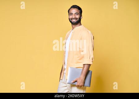 Happy confident indian business man holding laptop standing isolated on yellow. Stock Photo