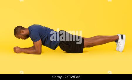 Sporty Black Man Doing Elbow Plank Exercise Over Yellow Background Stock Photo