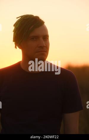 Young handsome man with dreadlocks posing against sky on sunset Stock Photo