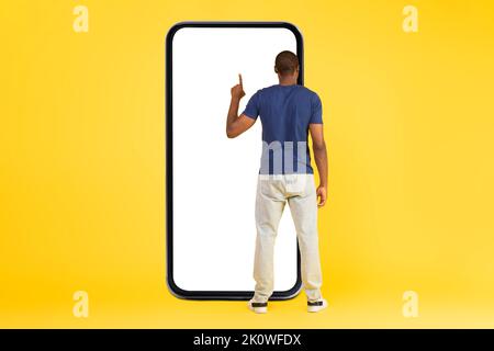African Man Using Large Smartphone Over Yellow Background, Back View Stock Photo