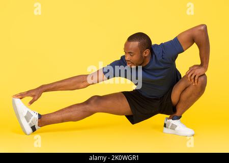Sporty Black Male Doing Stetching Exercise Touching Toe, Yellow Background Stock Photo