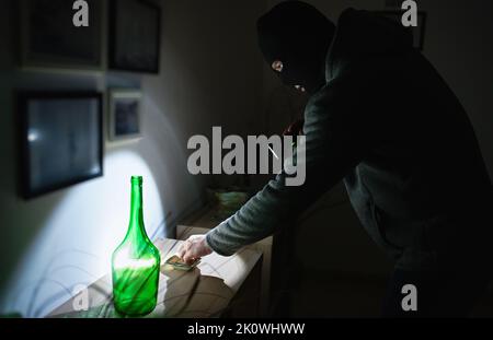 Masked robber with flashlight torch checking apartment. Stock Photo