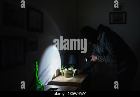 Masked robber with flashlight torch checking apartment. Stock Photo