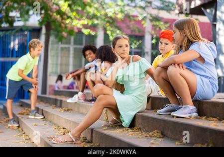Happy tweenagers friends sitting on steps outdoors and chatting Stock Photo