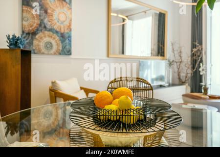 Designer metal fruit bowl filled with oranges and lemons on a round glass table in a decorated living room Stock Photo