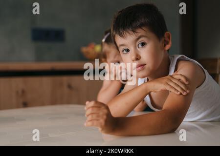 Cute small little boy with his baby sister waiting for food, enjoy happy childhood at home. Waiting for dinner or breakfast, family enjoying weekend Stock Photo
