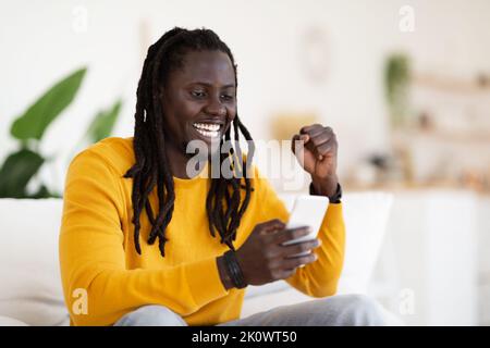 Great News. Joyful Black Man Reading Nice Message On Smartphone At Home Stock Photo