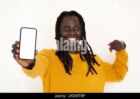 Online Offer. Cheerful Black Guy Pointing At Blank Smartphone In His Hand Stock Photo