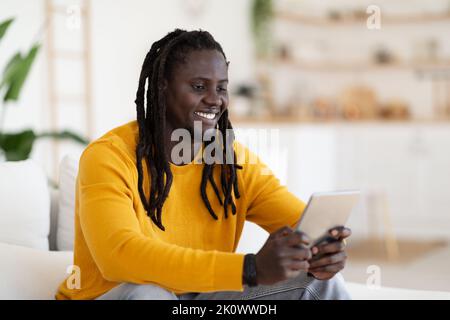 Cheerful Black Man Playing Game On Digital Tablet While Relaxing At Home Stock Photo