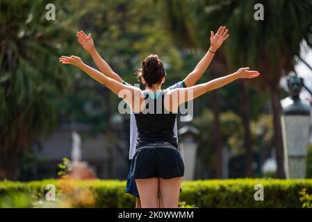 Couple doing yoga pose with arms raised at Praça da Liberdade in Belo Horizonte, Brazil. Stock Photo