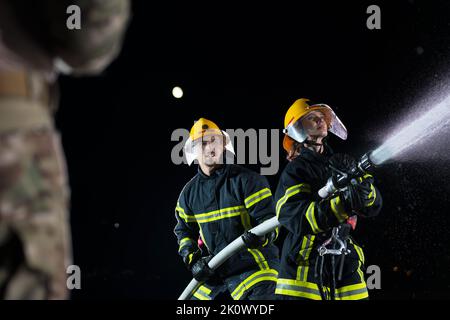 Firefighters using a water hose to eliminate a fire hazard. Team of female and male firemen in dangerous rescue mission.  Stock Photo