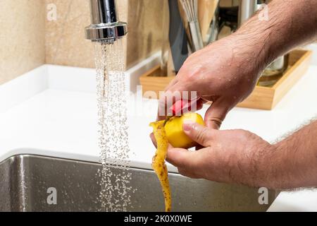 Close-up of male hands peeling potatoes with a potato peeler Stock Photo