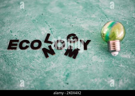 economy vs ecology conceptual image with the two words merging into each other next to green lightbulb on green background Stock Photo
